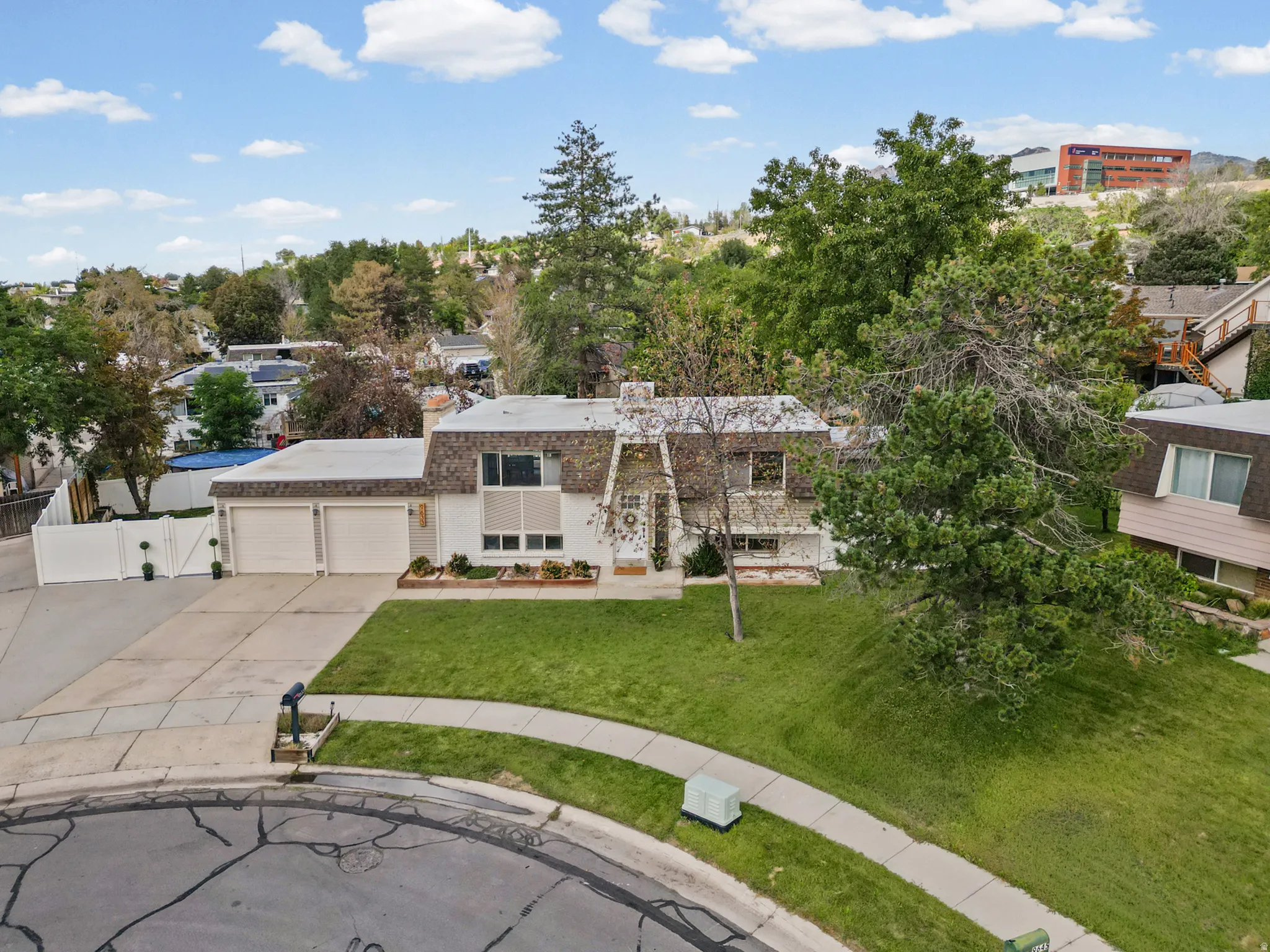 Two-car garage with white doors, expansive paved driveway, and established front landscaping