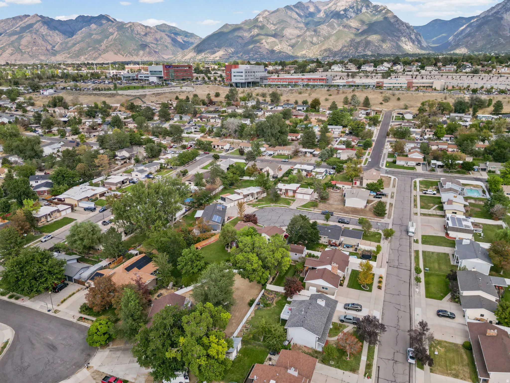 Aerial perspective showcasing a residential neighborhood with a mountainous backdrop, mature trees, and paved streets