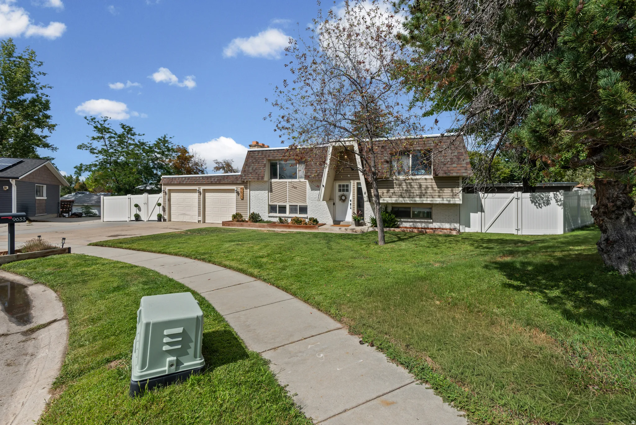 Split-level residence featuring a two-car garage, white fencing, and a concrete pathway
