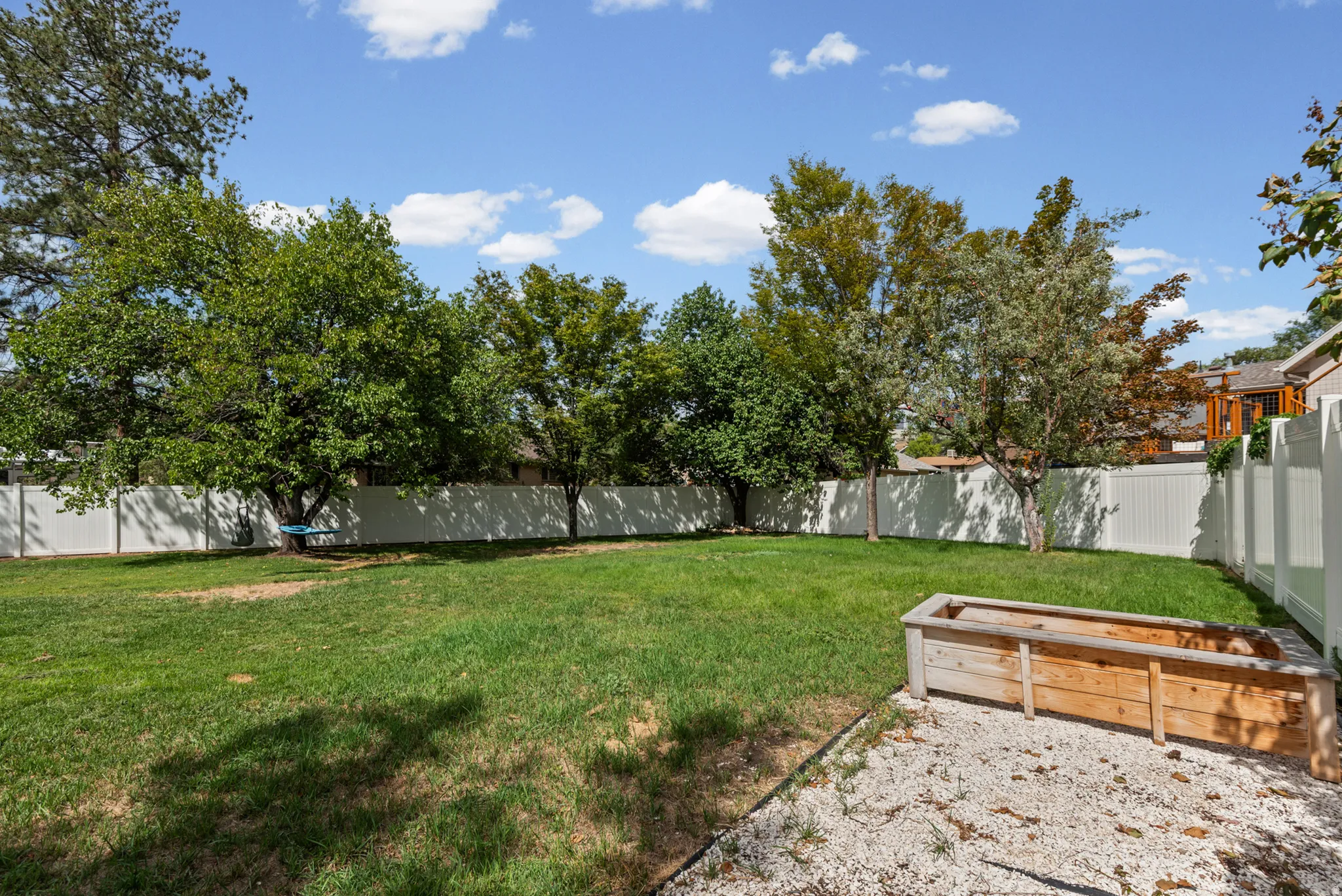 Expansive backyard featuring a manicured lawn, mature trees, white privacy fencing, and a wooden planter box