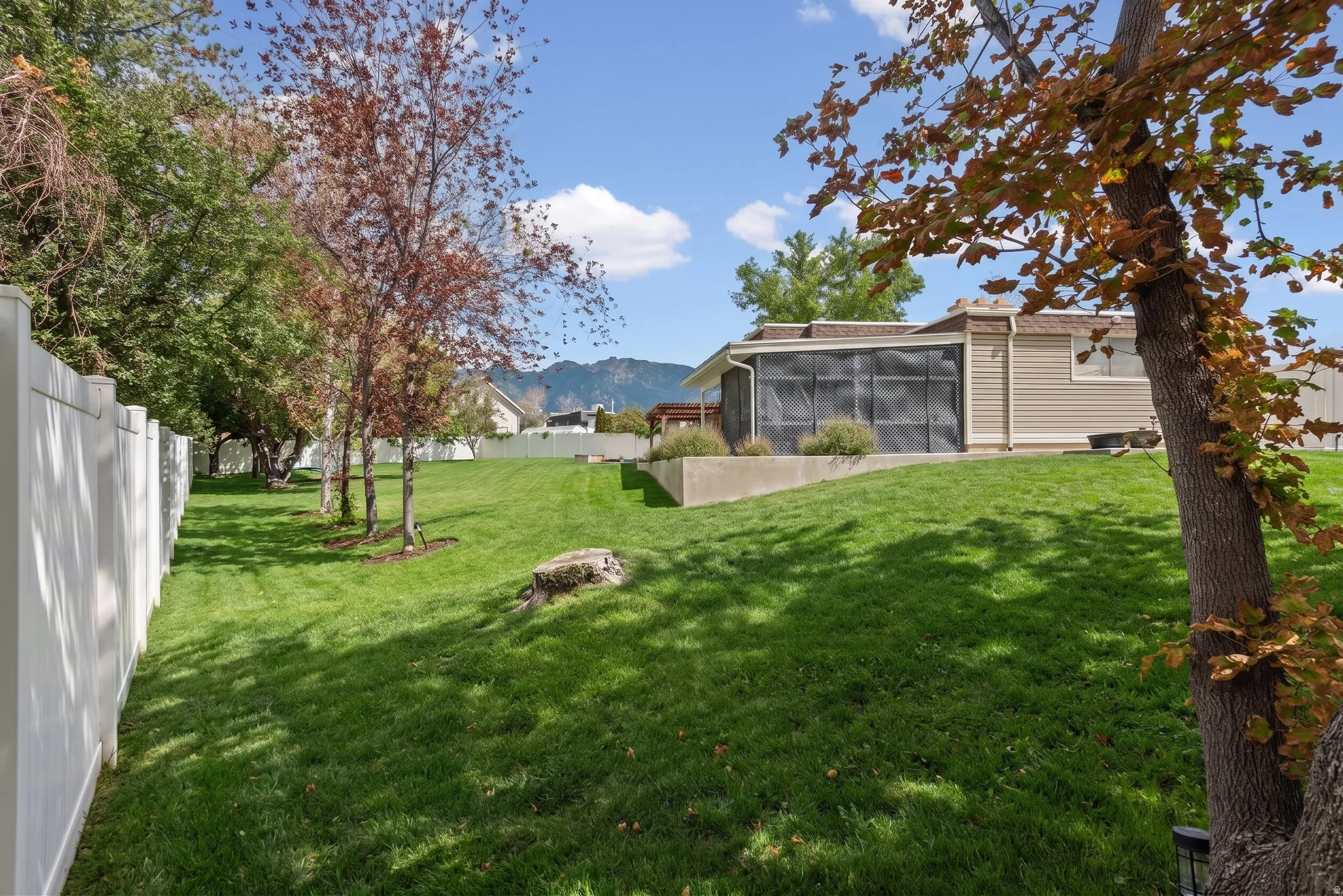 Expansive lawn area, mature trees, white privacy fencing, screened enclosure, and a raised planter bed