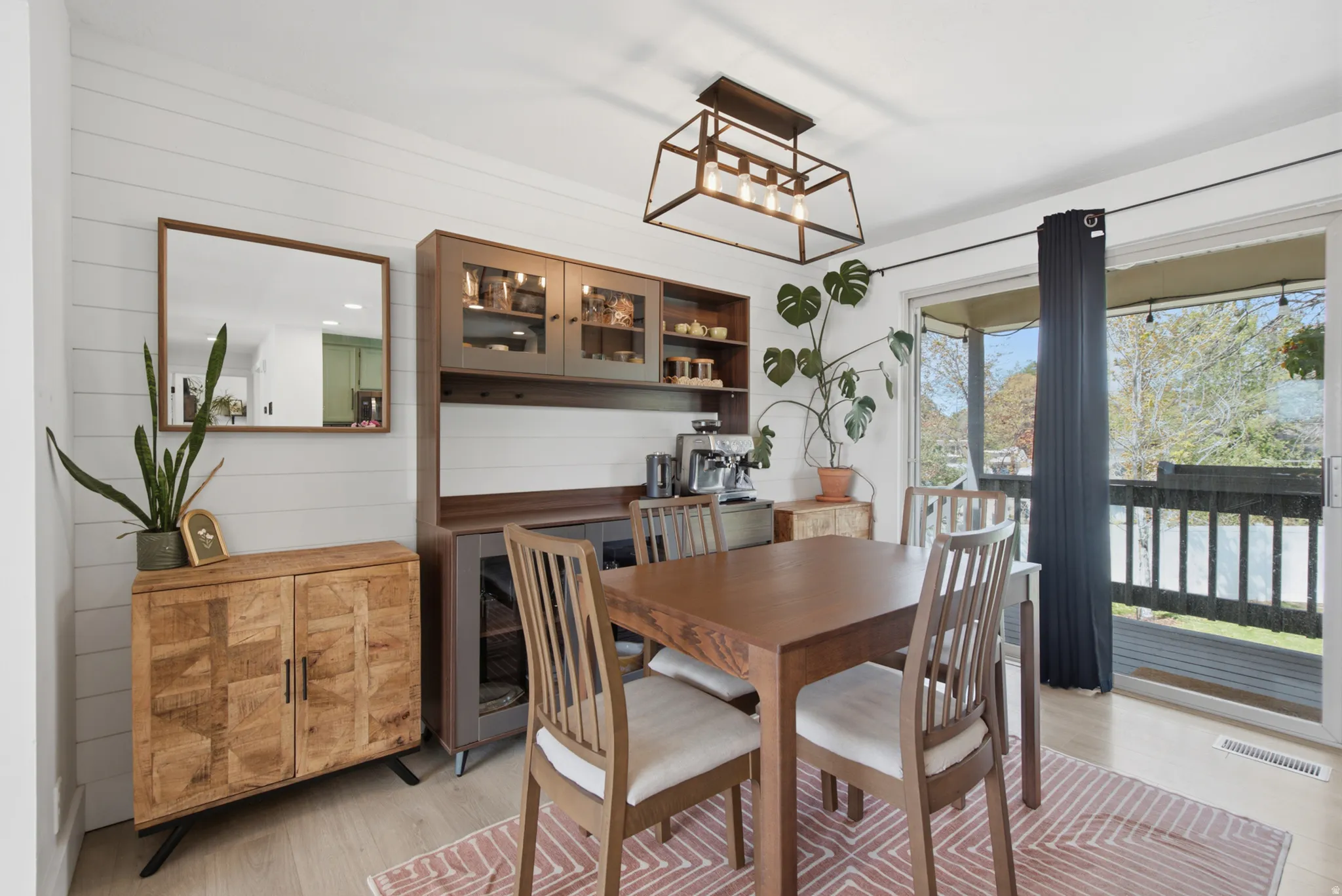 Shiplap accent wall, built-in cabinetry with glass-front doors, modern ceiling light fixture, wood-finish flooring, and sliding glass door