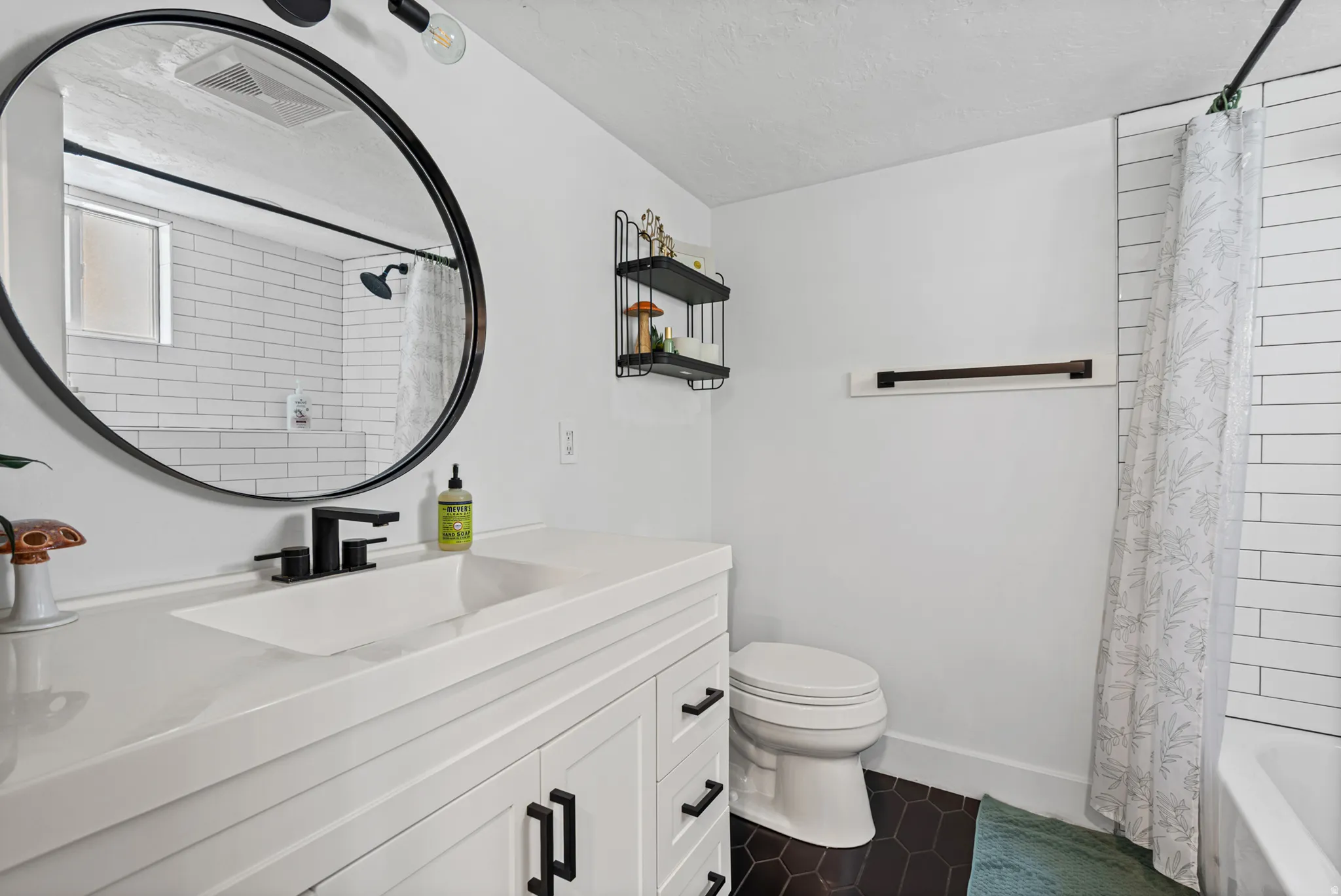 Bathroom featuring a white vanity with integrated sink, black fixtures, and a circular mirror
