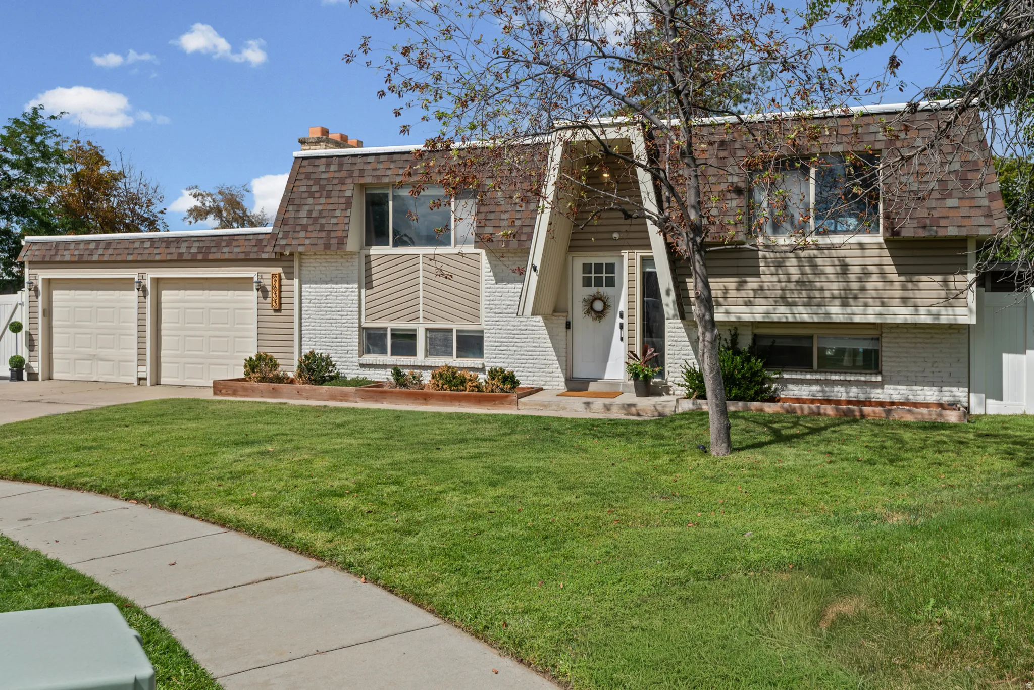 Split-level residence featuring a two-car garage, white brick facade, and wood-finish siding