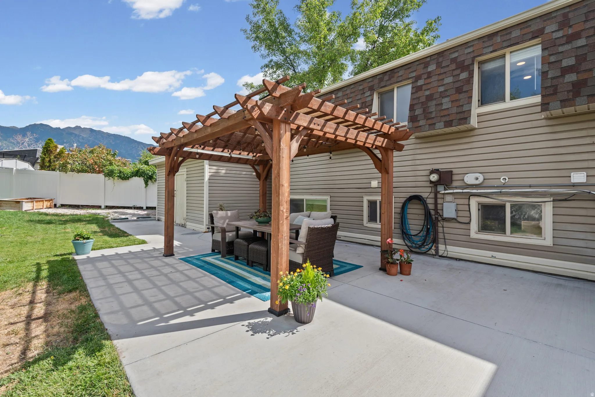 Expansive concrete patio with a wooden pergola, leading to a manicured lawn area