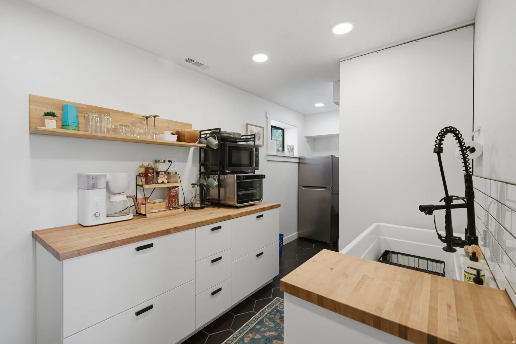 White cabinetry with wood-finish countertops, subway tile backsplash, and a deep utility sink with a matte black faucet