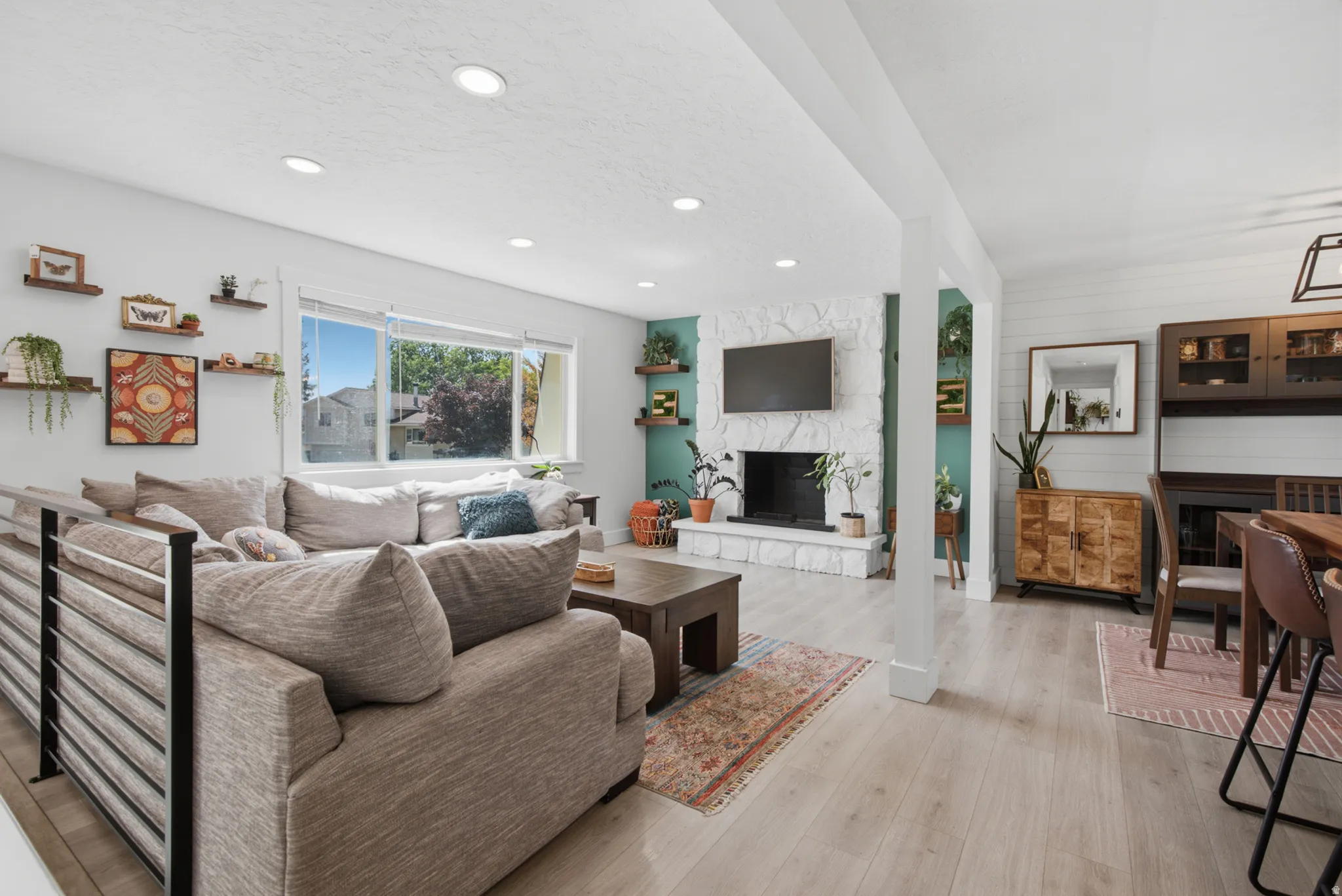 Light wood-finish flooring throughout, recessed ceiling lighting, white stone fireplace, integrated shelving, and shiplap wall accent