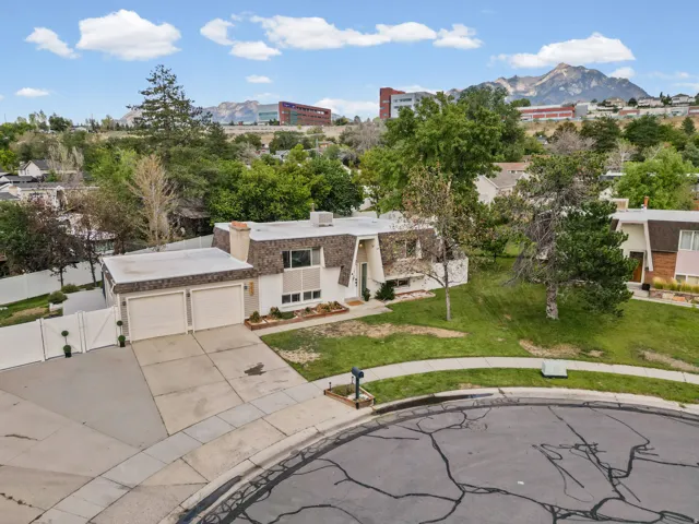 Two-car garage with concrete driveway, mature landscaping, and a sloped front lawn