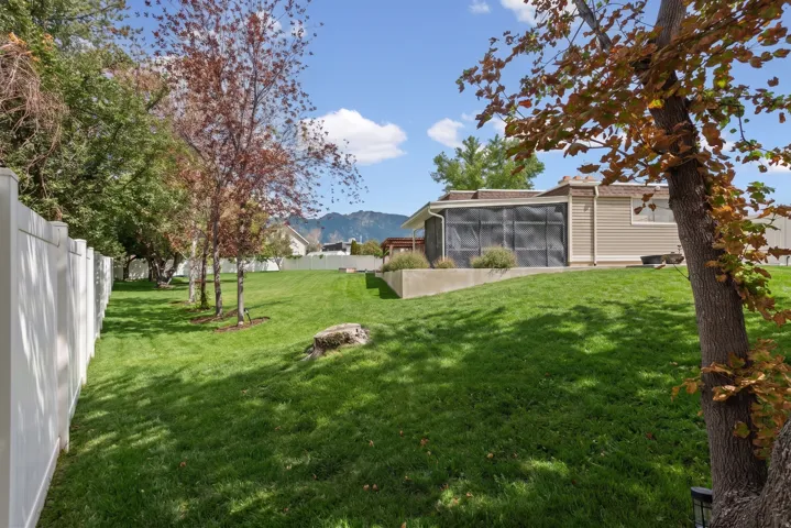 Expansive lawn area, mature trees, white privacy fencing, screened enclosure, and a raised planter bed