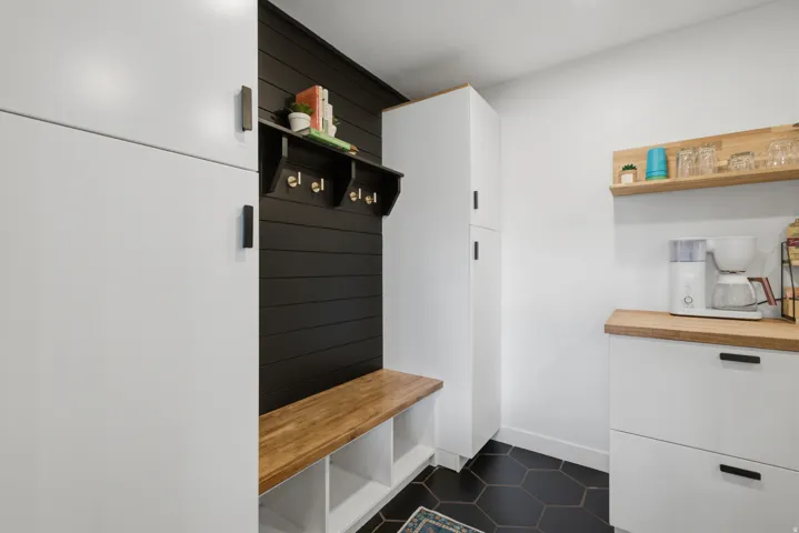 Integrated storage cabinetry with matte black hardware, black shiplap accent wall, natural wood-finish bench with cubby storage, hexagon floor tiling, and natural wood-finish floating shelves