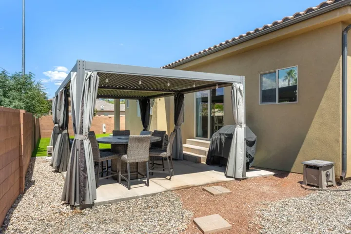 Enclosed patio featuring a gray metal pergola with adjustable louvered roof and privacy curtains, alongside a concrete block wall and gravel landscaping