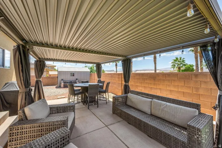 Expansive covered patio with string lighting, privacy curtains, and a concrete paver surface