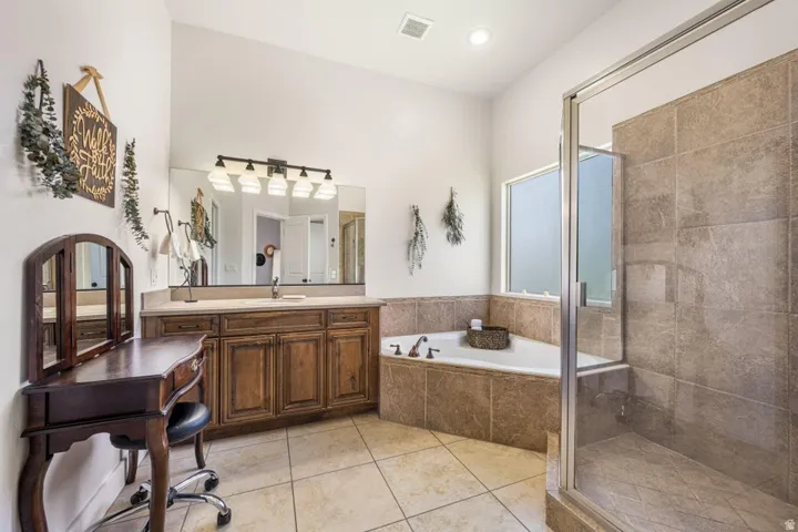 Spacious bathroom featuring a dual vanity with wood cabinetry, a walk-in shower with glass enclosure, a built-in corner soaking tub, and tile flooring