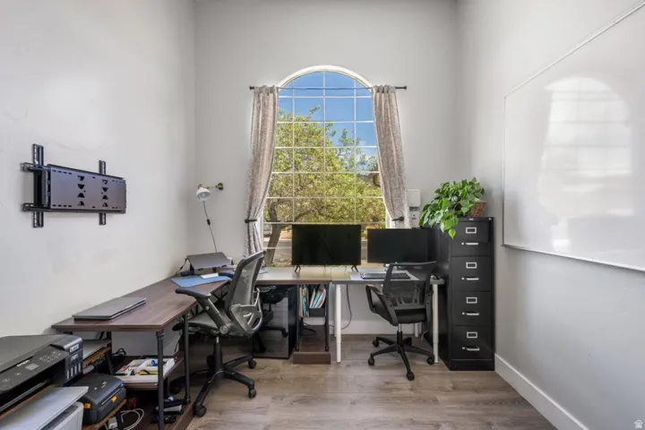 Arched window with drapery, wood-finish flooring, white wall-mounted board, and a wall-mounted television bracket