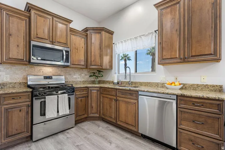 Wood-finish cabinetry paired with granite countertops, a tiled backsplash, stainless steel appliances, and wood-finish flooring