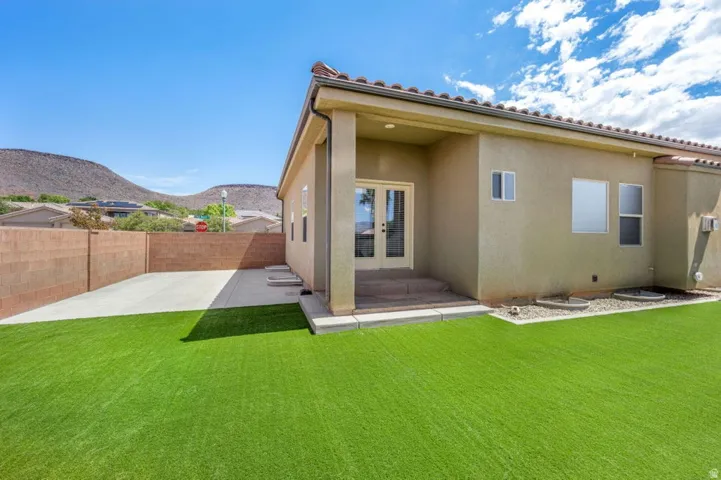 Expansive green turf area, covered patio, French doors, paved concrete patio, and stucco exterior