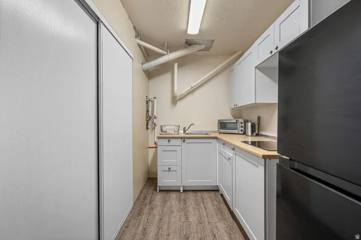 Compact kitchen area featuring white shaker-style cabinetry, wood-finish countertops, and a black refrigerator