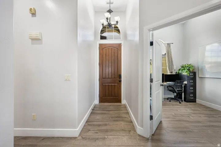 Wood-finish flooring throughout, solid wood entry door with arched transom window, and a multi-light chandelier