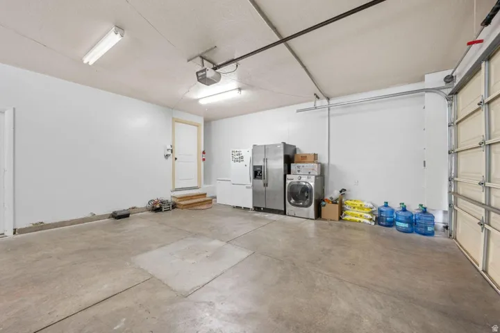 Concrete flooring, white painted walls, exposed ceiling, double fluorescent lighting, and a white interior door
