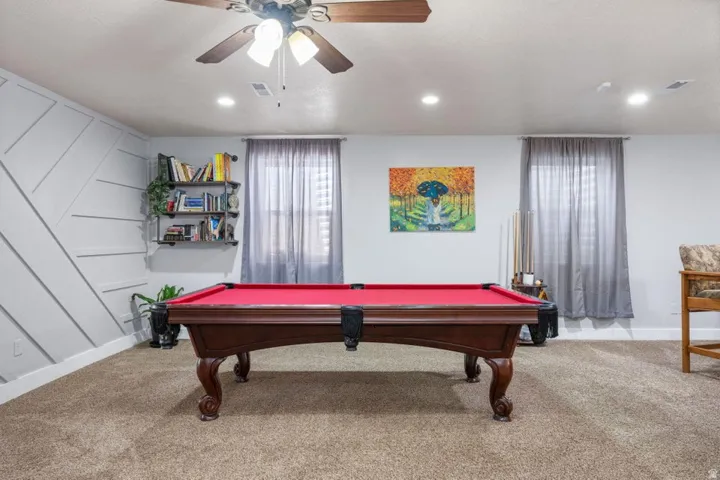 Recessed lighting, ceiling fan, textured accent wall, two windows with drapery, and carpeted flooring