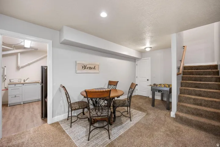Carpeted staircase with wood handrail, recessed lighting, and an adjacent utility room with wood-finish flooring and light-colored cabinetry