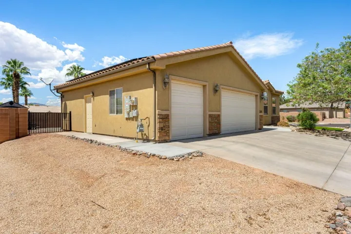 Stucco exterior with stone accents, two-car garage, concrete driveway, and side gate access