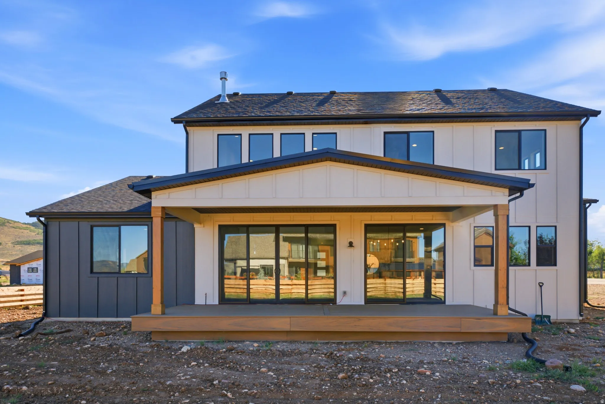 Rear exterior featuring a covered deck, board-and-batten siding, multiple windows, and a shingled roof
