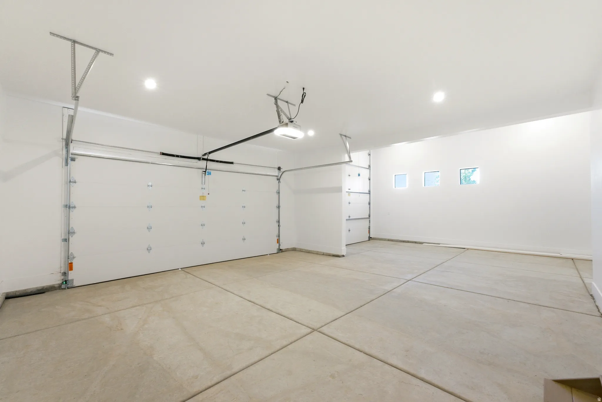 Spacious garage featuring a concrete floor, three transom windows, a white sectional garage door, and recessed lighting