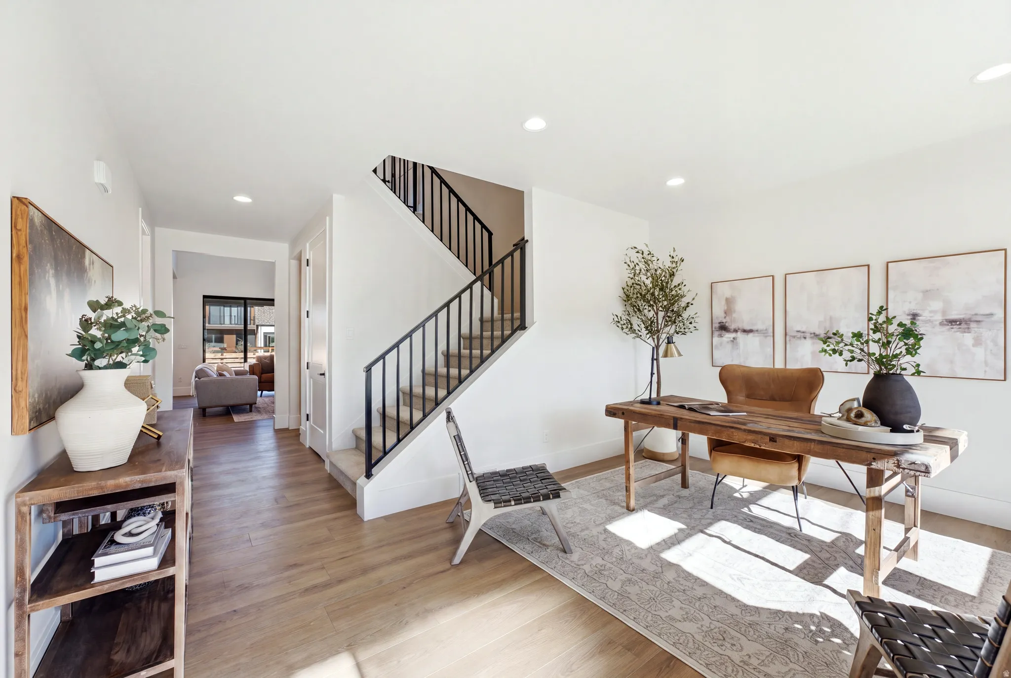 Hardwood-style flooring throughout, recessed lighting, and a staircase with black metal railings