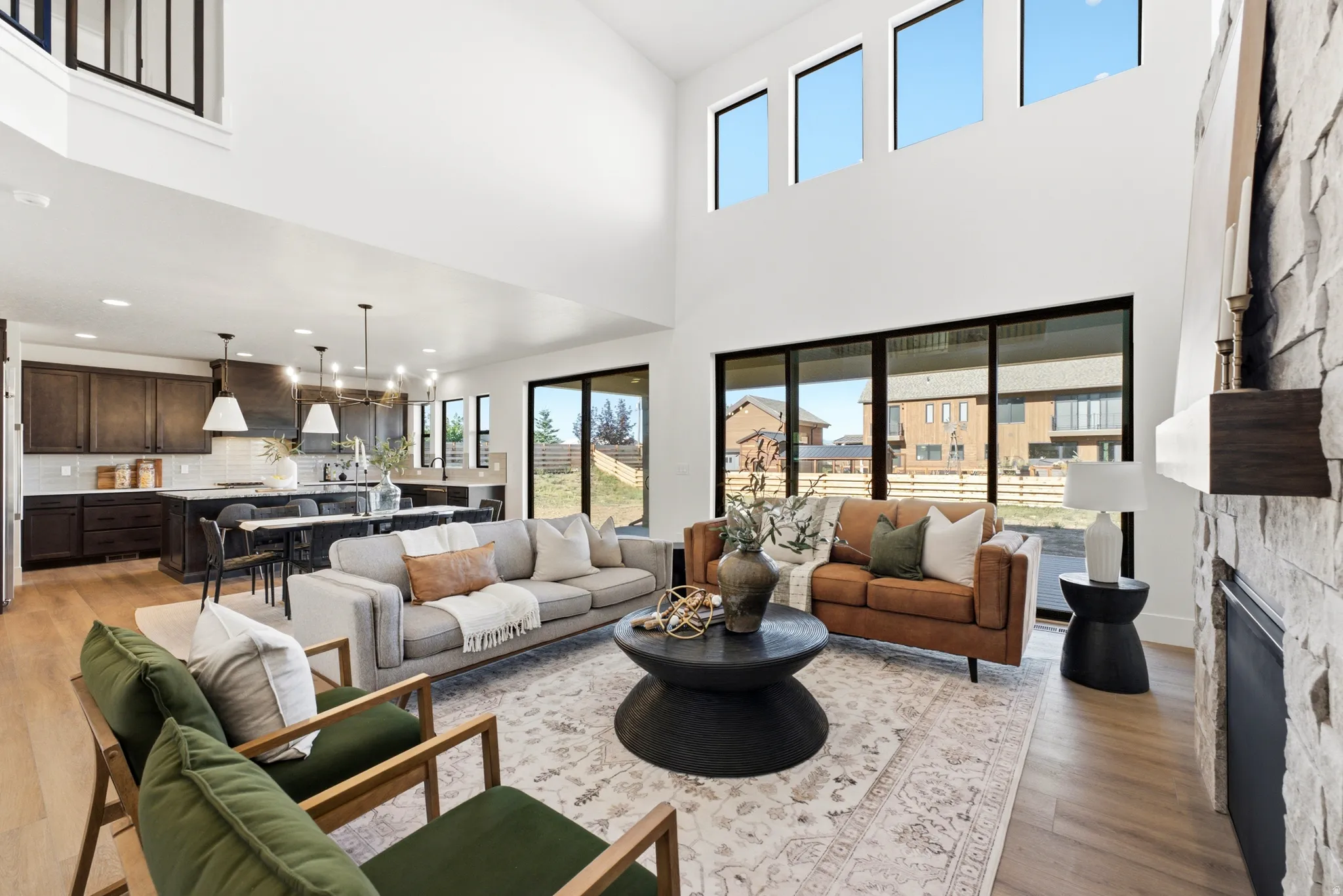 Soaring ceilings with upper transom windows, a stone-clad fireplace, wood-finish flooring, and expansive glass sliding doors