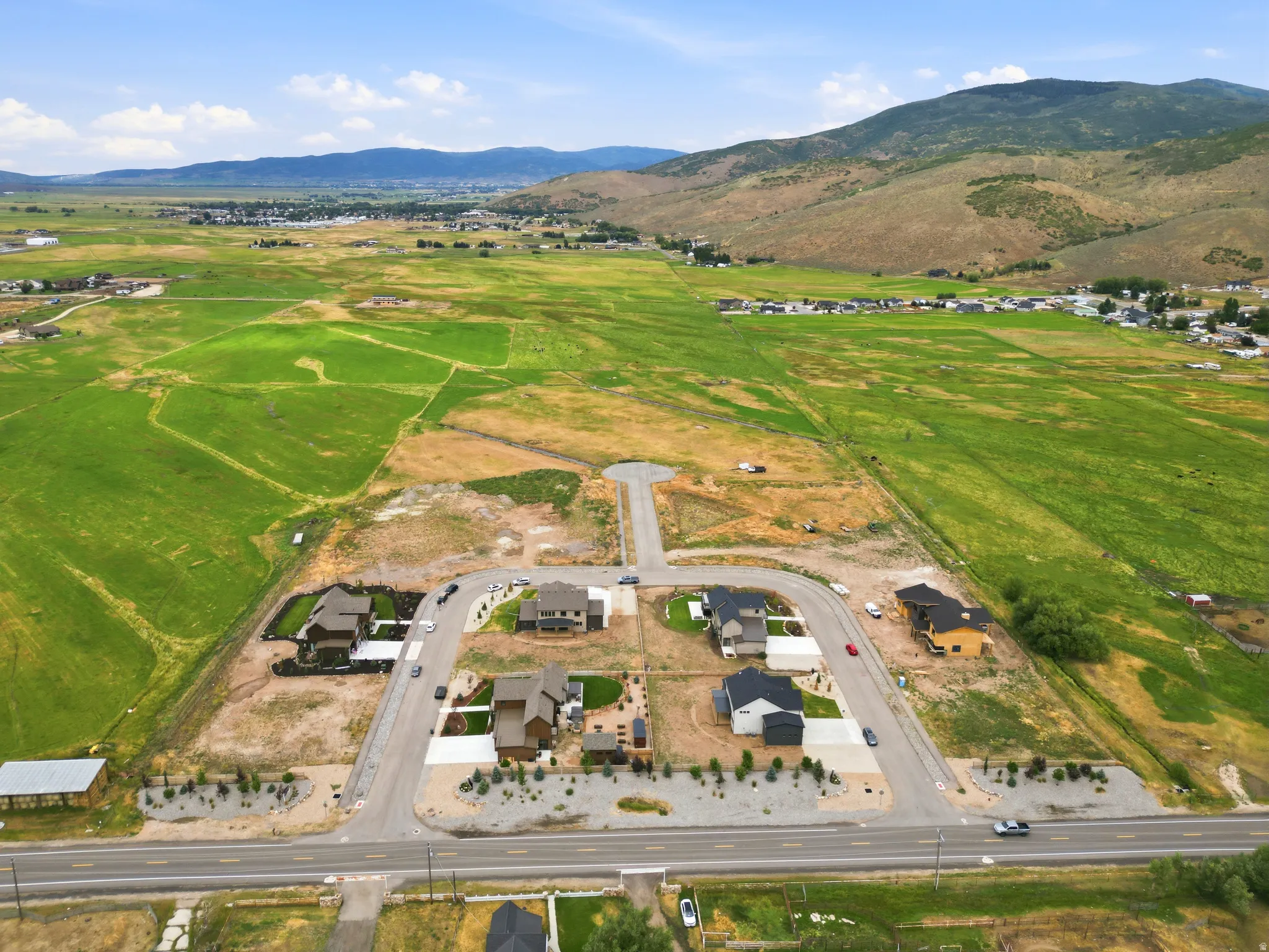 Developing residential area with mountain backdrop, surrounding green fields, and paved roadways