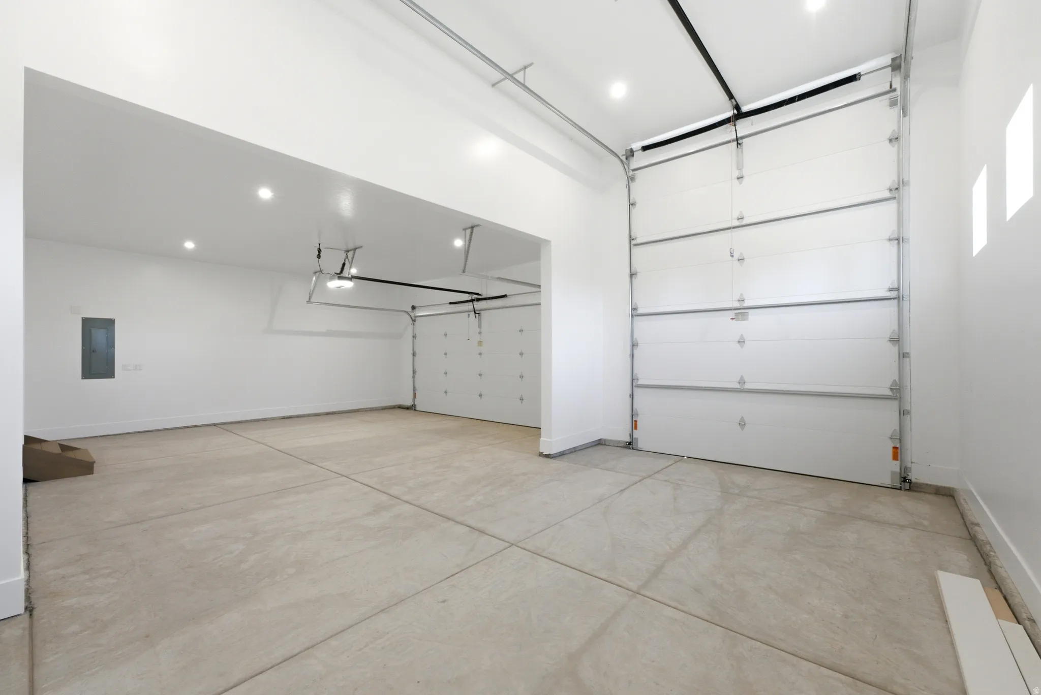 Expansive garage with multiple overhead doors, concrete flooring, recessed lighting, and white painted walls