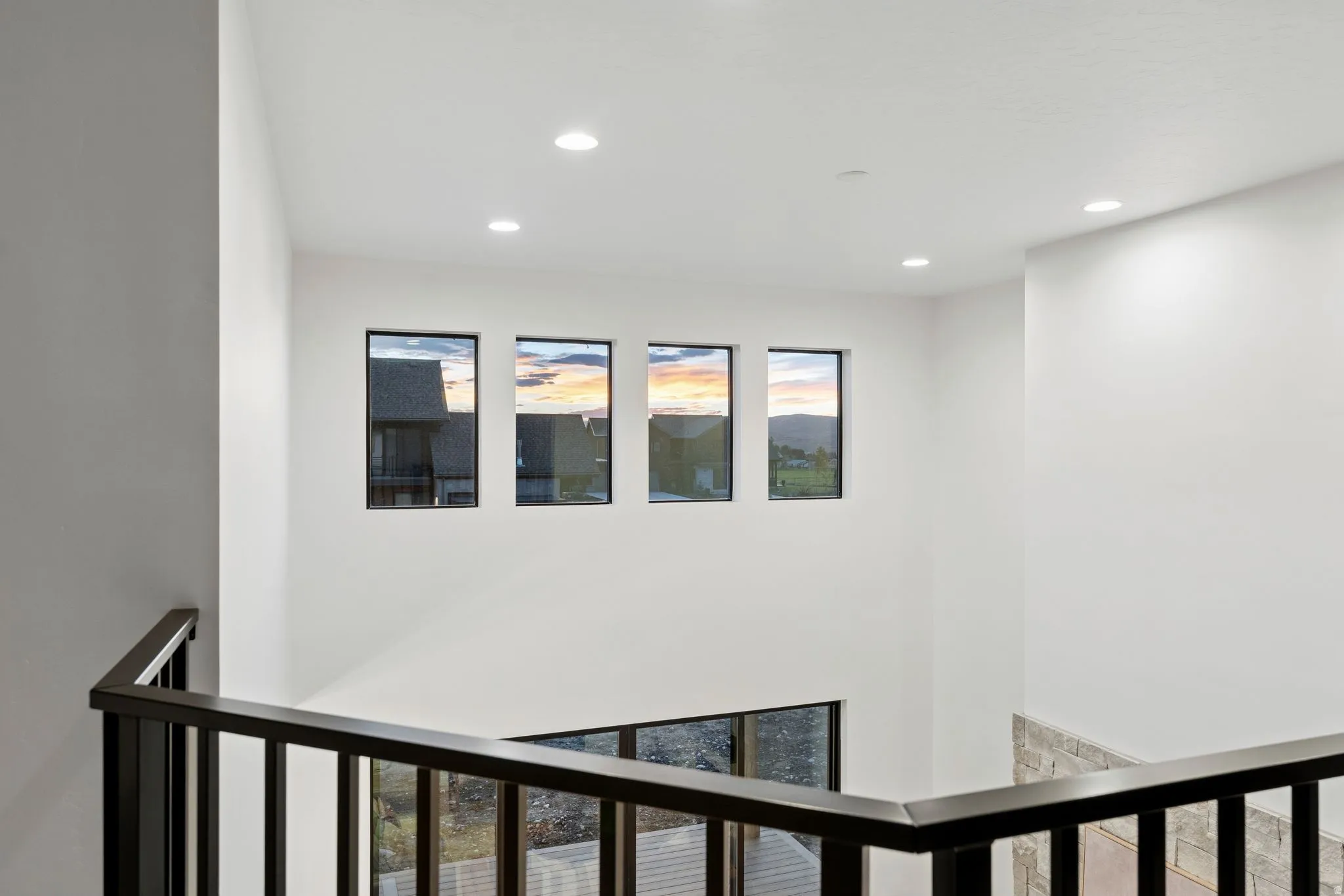 High ceilings featuring recessed lighting, a modern black metal railing, and multiple windows providing natural light