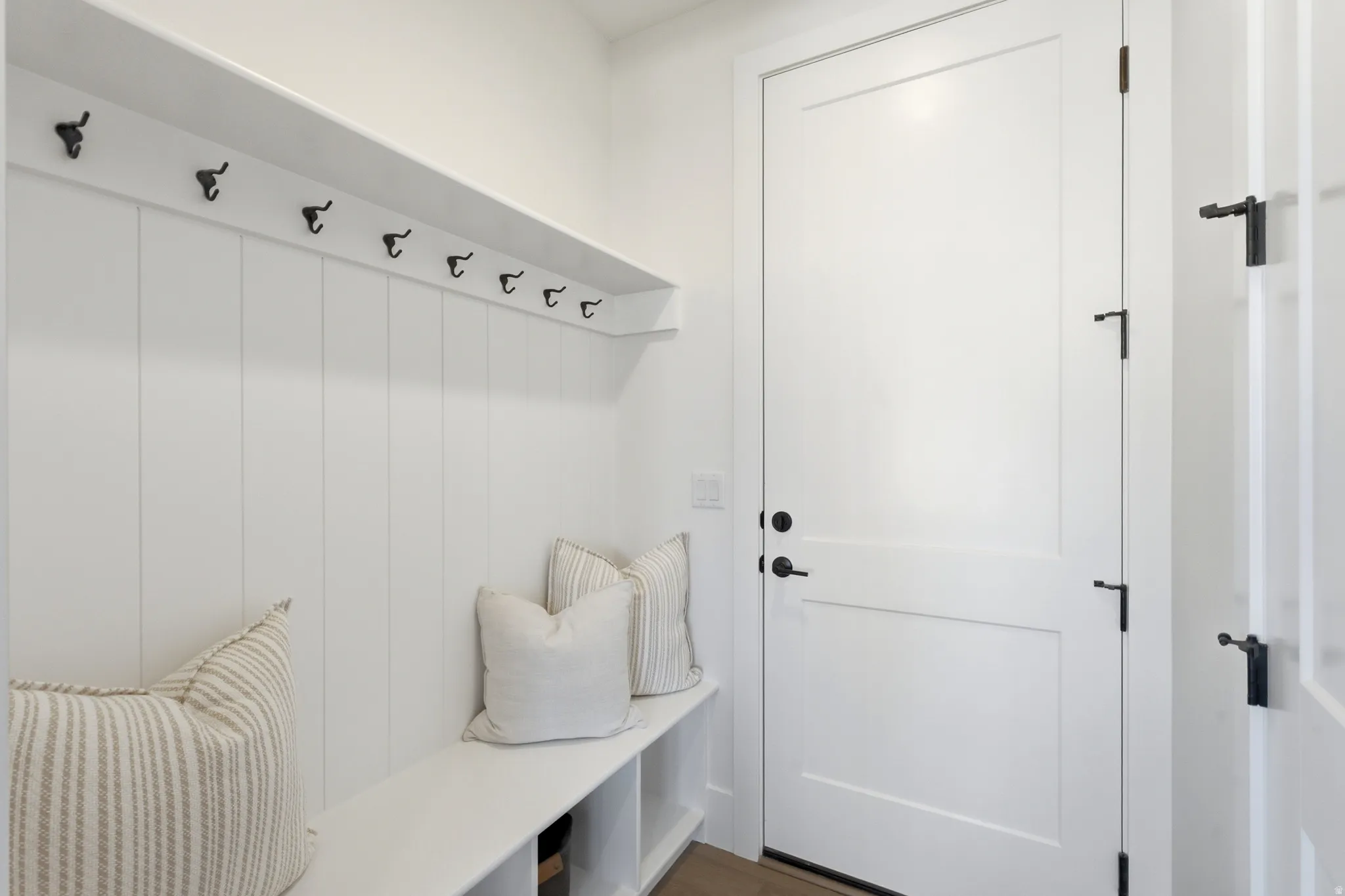 Built-in bench with storage, vertical paneling, integrated shelf, and multiple coat hooks