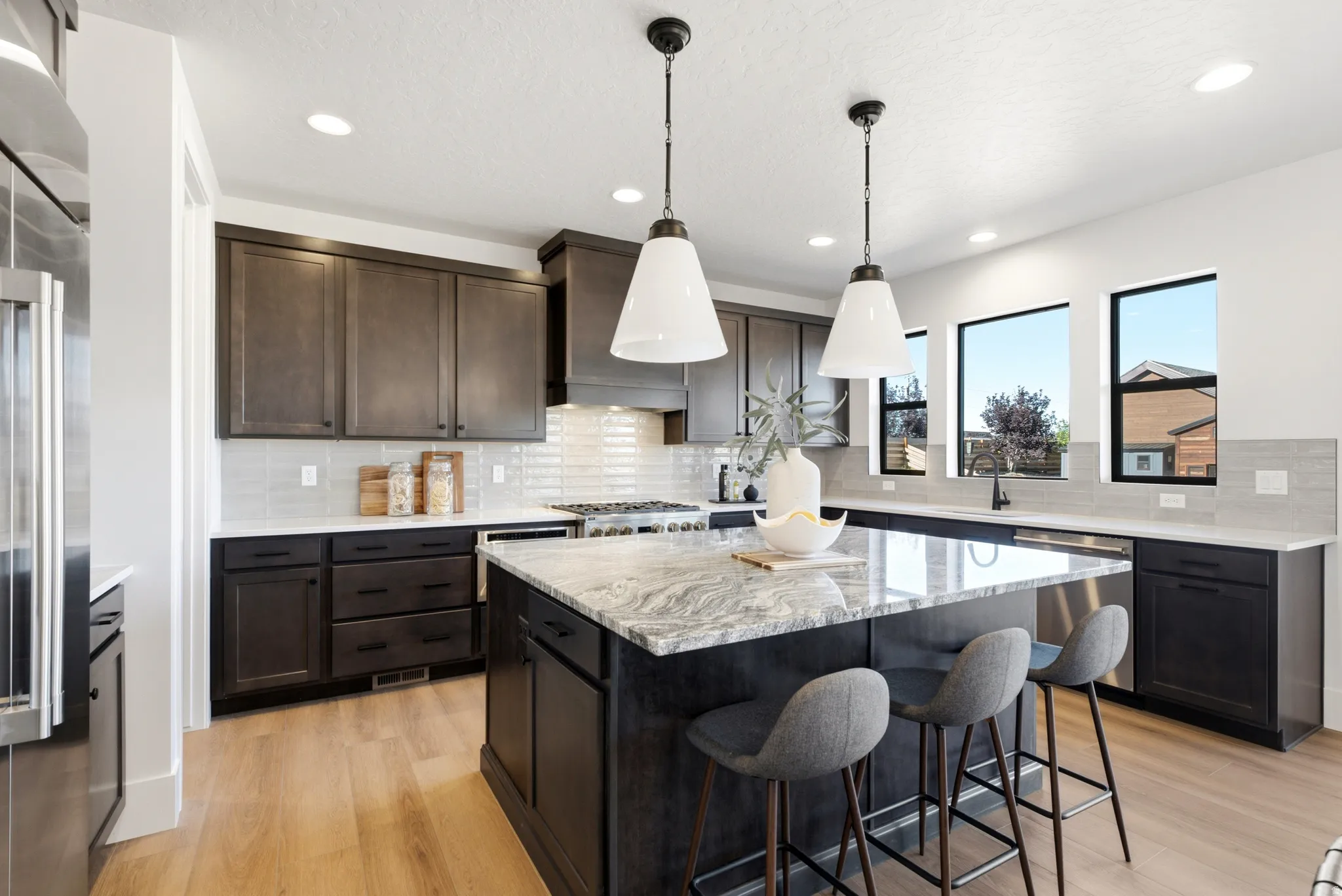 Kitchen featuring dark cabinetry, a large center island with a light-toned stone surface, wood-finish flooring, and recessed lighting