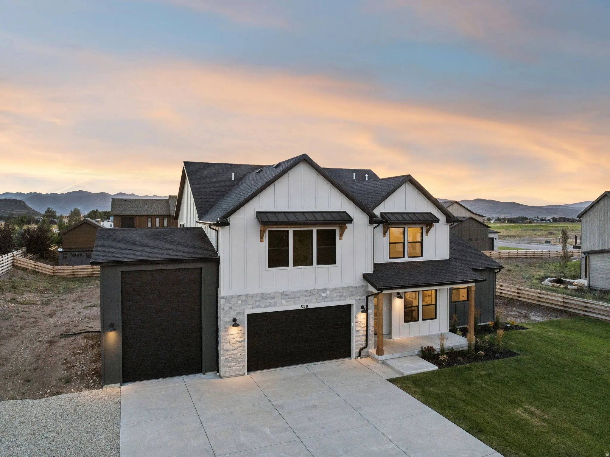 White vertical siding facade with stone accents, black-trimmed windows, and a two-car garage