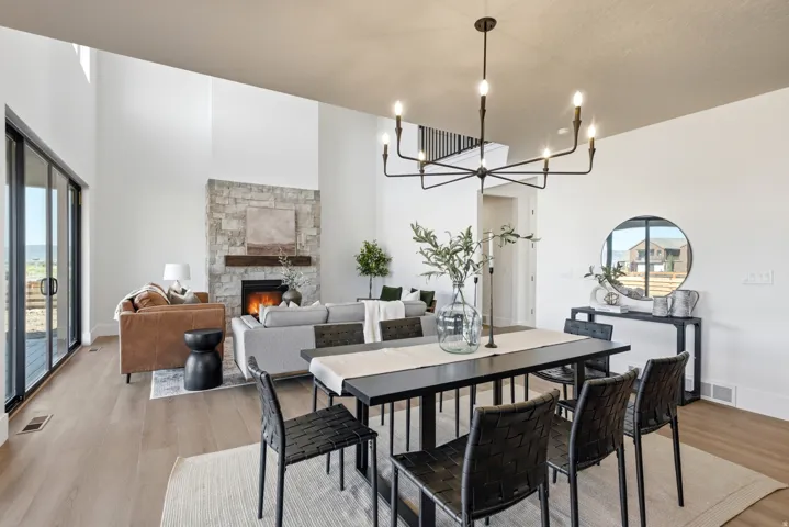 High ceilings, wood-finish flooring, stone-clad fireplace with wood mantel, large sliding glass doors, and a modern chandelier