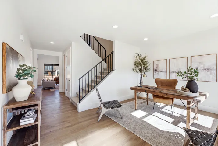 Hardwood-style flooring throughout, recessed lighting, and a staircase with black metal railings