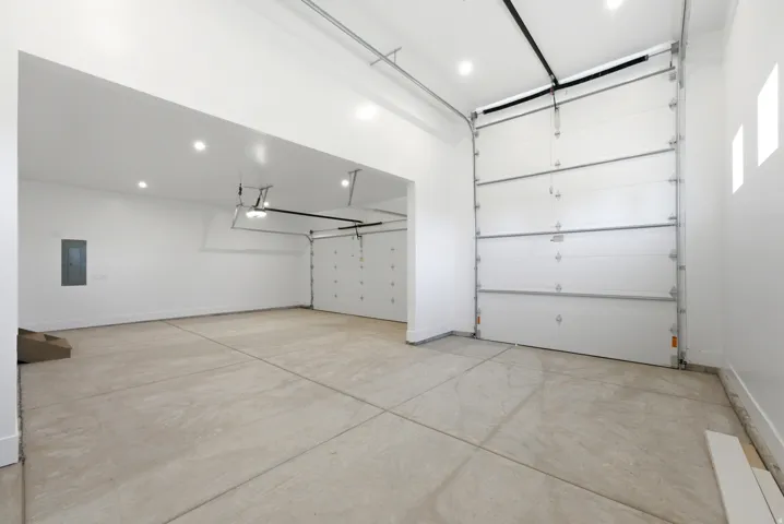Expansive garage with multiple overhead doors, concrete flooring, recessed lighting, and white painted walls