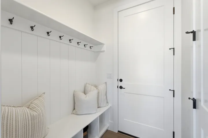 Built-in bench with storage, vertical paneling, integrated shelf, and multiple coat hooks