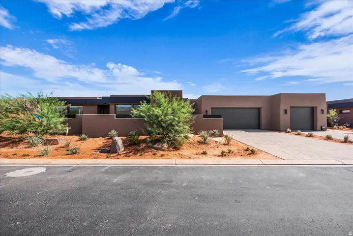 Contemporary stucco exterior with dark garage doors, expansive driveway, and low-maintenance landscaping
