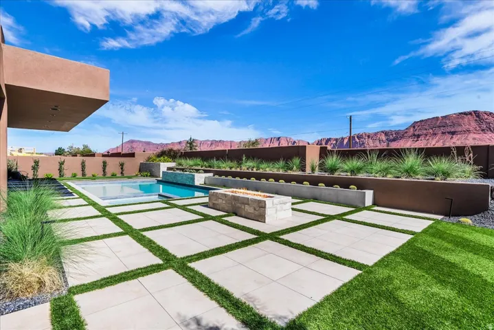 Outdoor living area featuring a swimming pool, integrated spa, fire pit, and stone paver patio with artificial turf accents