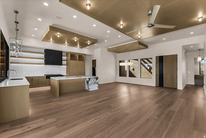 Wood-finish flooring throughout, kitchen with light wood-finish cabinetry, white subway tile backsplash, and a waterfall island with a stone slab