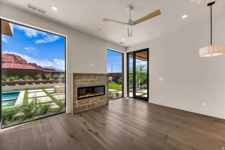 Wood-finish flooring, stone-clad fireplace with electric insert, expansive floor-to-ceiling windows, and contemporary ceiling fan