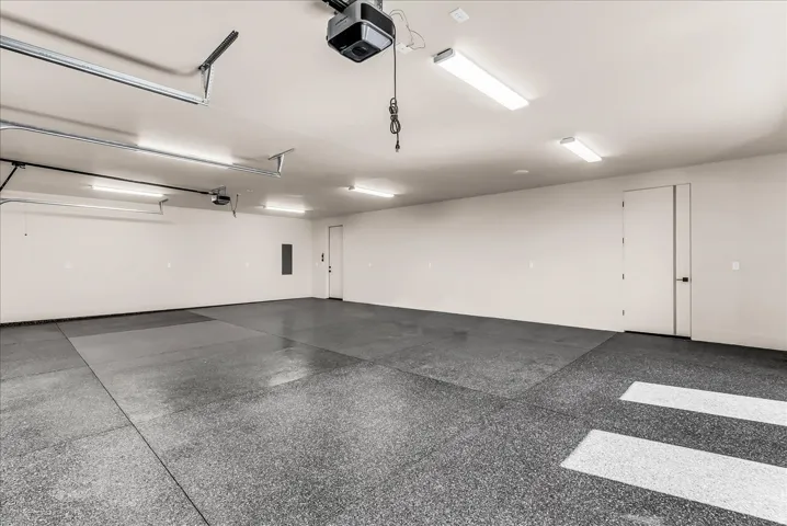 Spacious garage with an epoxy-coated floor, multiple fluorescent light fixtures, and two panel doors