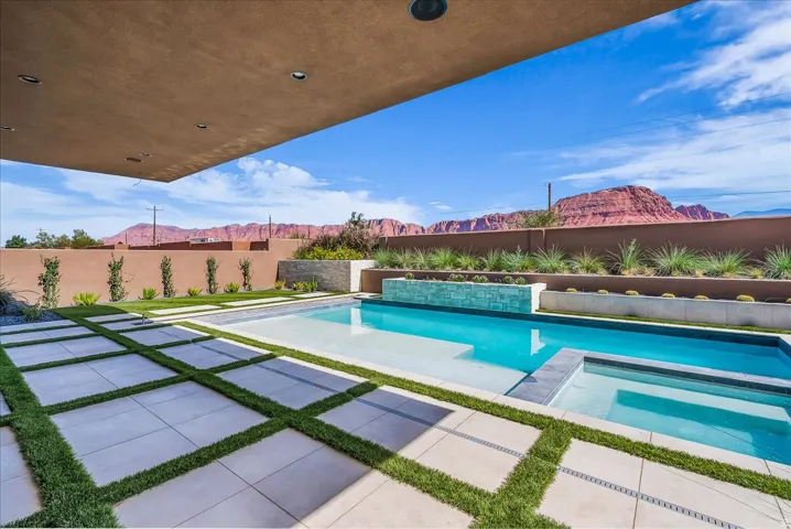 Expansive patio with integrated pool and spa, covered outdoor area with recessed lighting, and a perimeter wall with tiered landscaping
