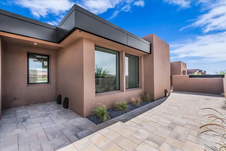 Contemporary stucco exterior with dark trim accents, paver pathway, integrated landscaping with decorative gravel, and large windows