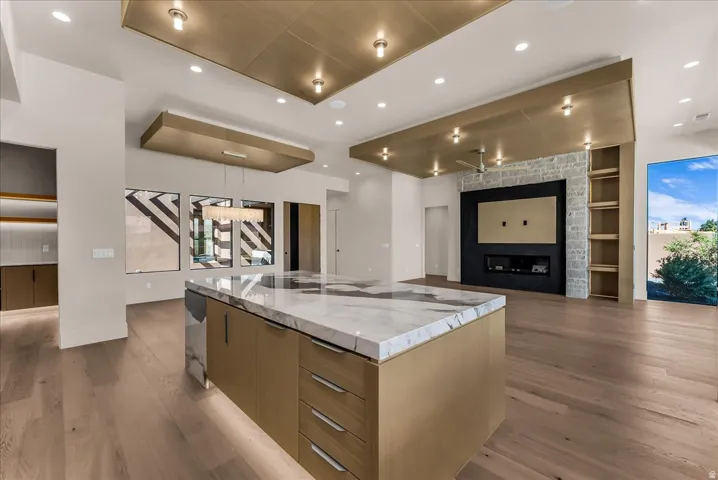 Open-concept living space with wood-finish flooring, a central island featuring a stone countertop, a built-in media wall with a fireplace, and integrated shelving