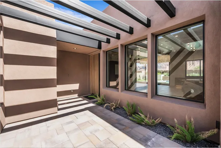 Contemporary stucco exterior with a covered entry, large windows, wood entry door, and decorative rock landscaping