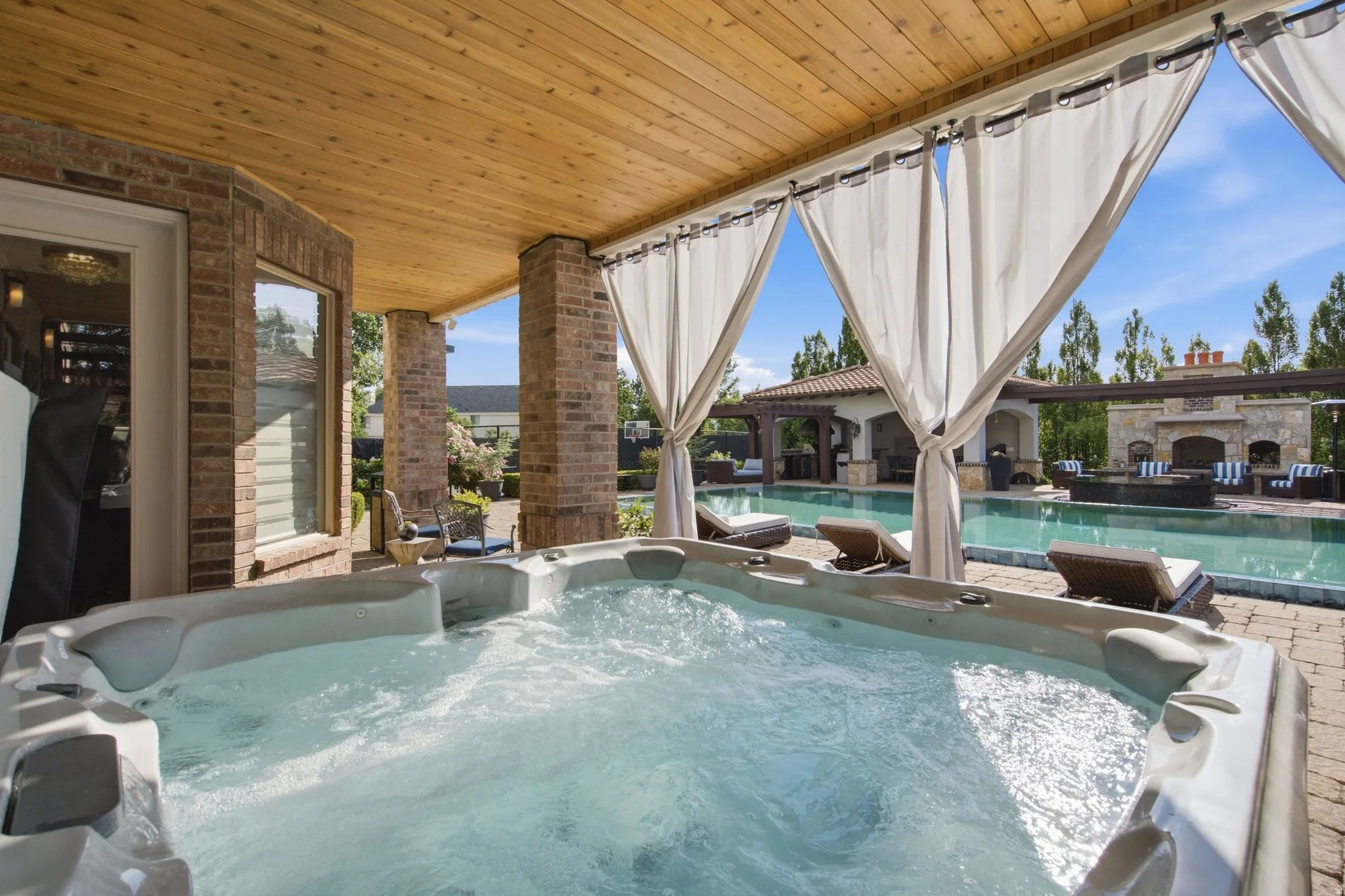 Covered patio with a built-in spa, wood-plank ceiling, and brick pillars